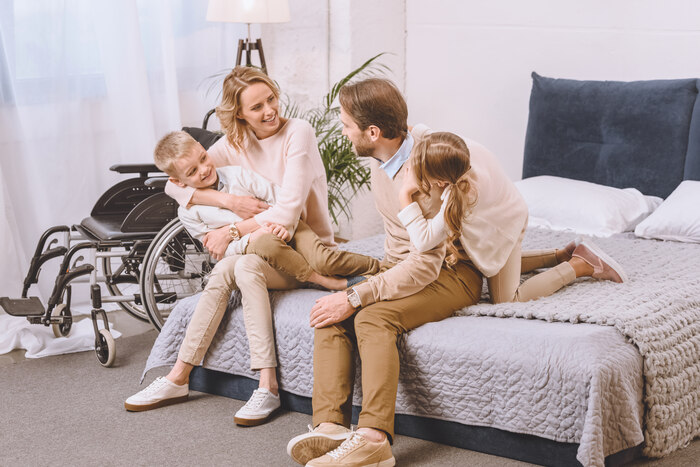 Specialist Disability Accommodation (SDA), father with disability and happy mother sitting with children on bed