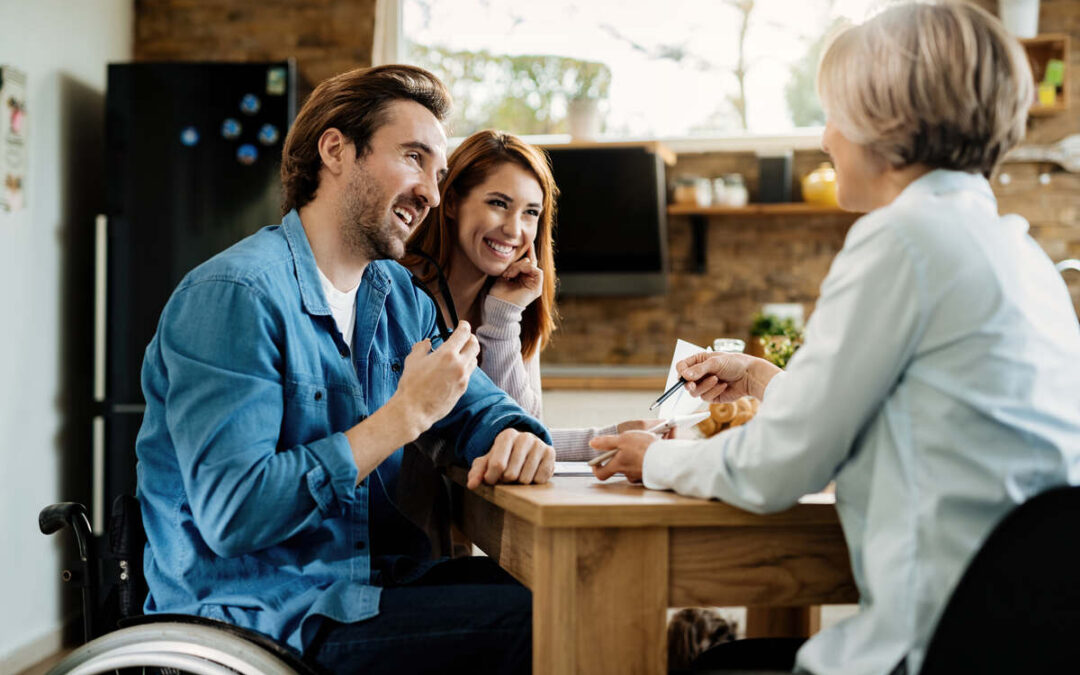 Medium Term Accommodation NDIS Capability Care - Happy man in wheelchair and his wife using digital tablet with their financial advisor during a meeting at home.