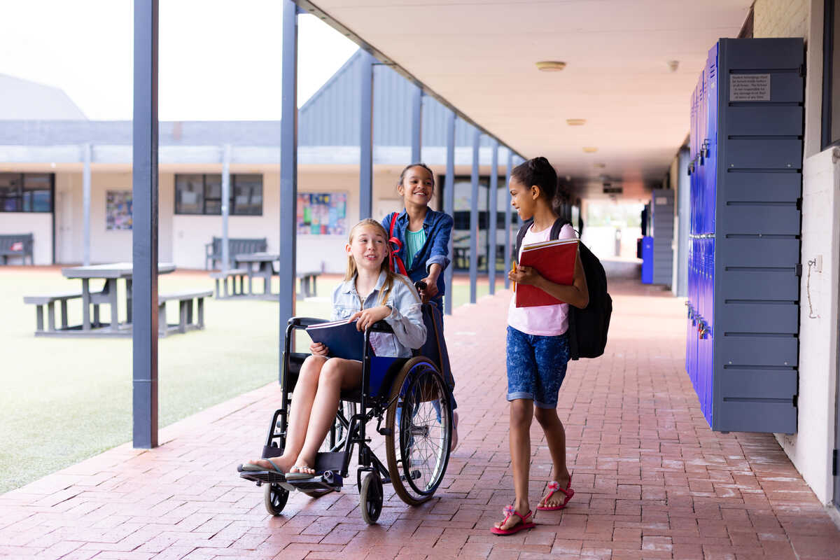 NDIS After School Care - Happy diverse schoolgirl in wheelchair with her friends in corridor at school. Education, inclusivity, school, learning and disability concept. 